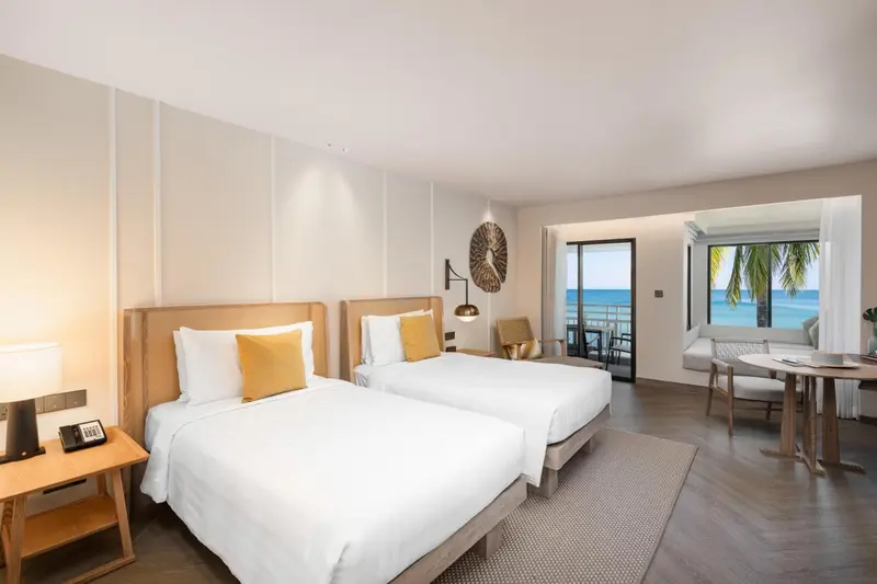 Chambre lumineuse avec deux lits simples et vue sur la mer.