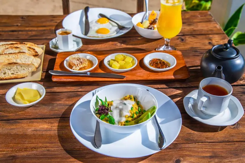 Une table en bois présente un copieux petit-déjeuner avec des œufs, des fruits et des viennoiseries.