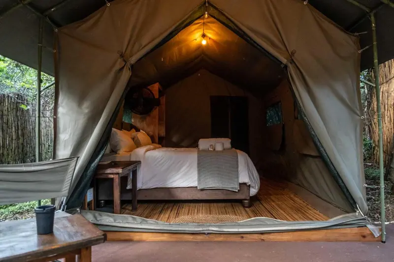 Une tente de safari aménagée en chambre avec un lit et une table de chevet.