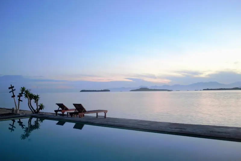 Transats au bord d'une piscine à débordement face à la mer au coucher du soleil.