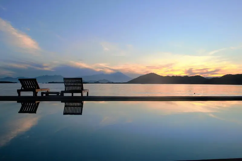 Deux chaises longues se reflètent dans l'eau d'une piscine au coucher du soleil.