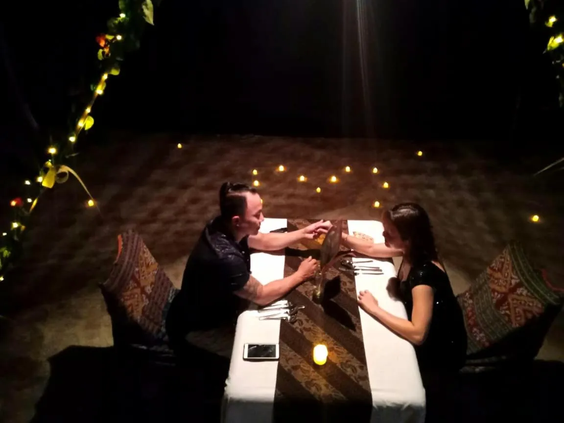 Un couple est assis à une table décorée pour un dîner romantique sur le sable.
