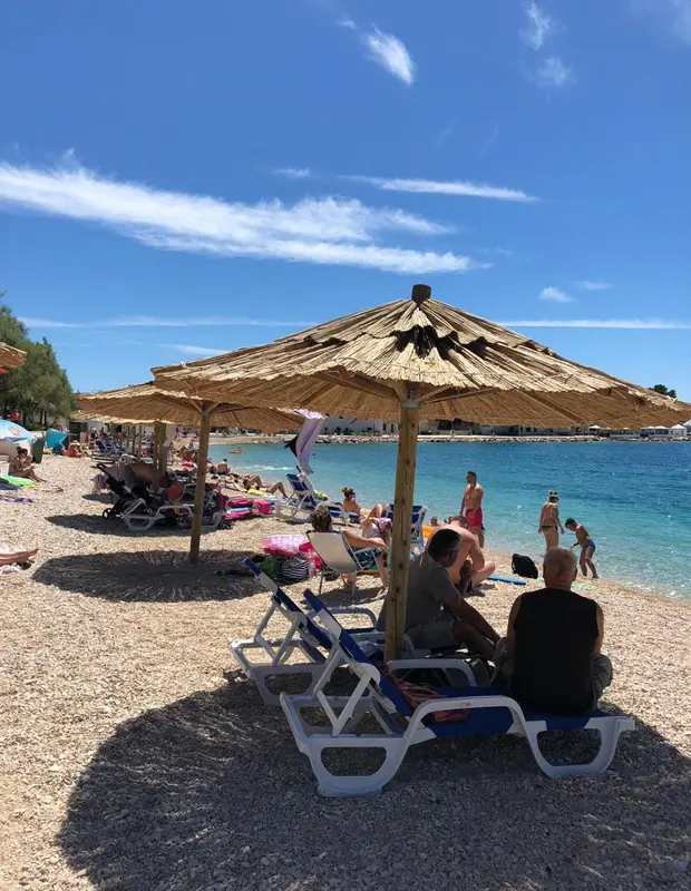 Transats et parasols sur une plage de galets au bord d'une mer turquoise.