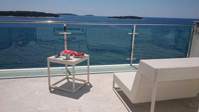Une table basse avec des fruits est posée sur une terrasse ensoleillée avec vue sur la mer.