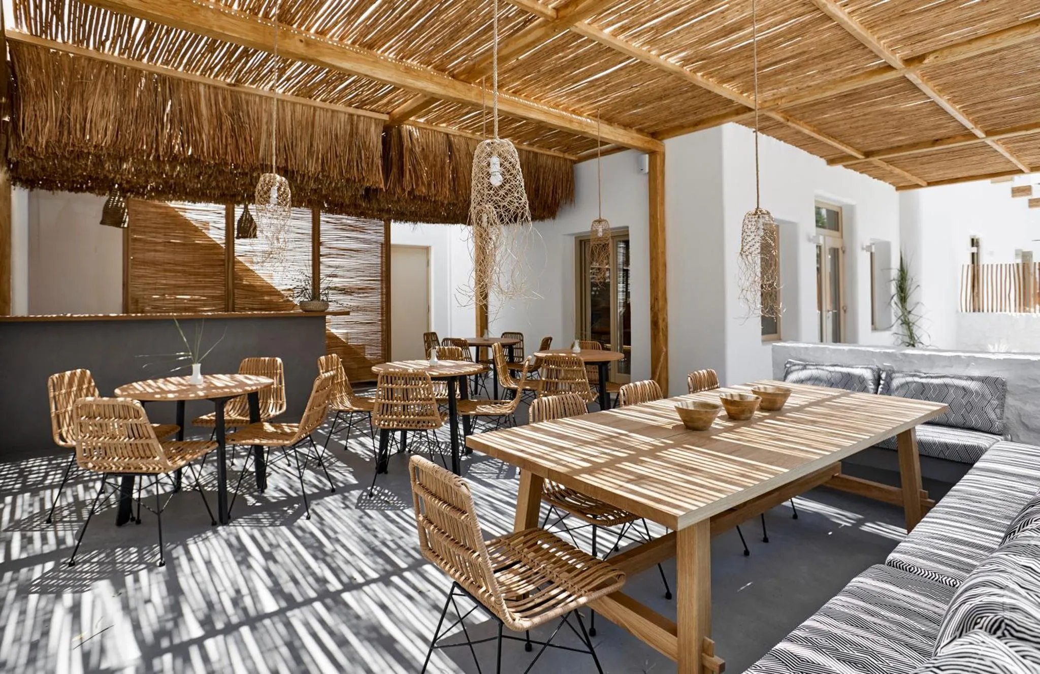 Une salle à manger lumineuse avec des tables en bois et des chaises en rotin sous un toit de chaume.