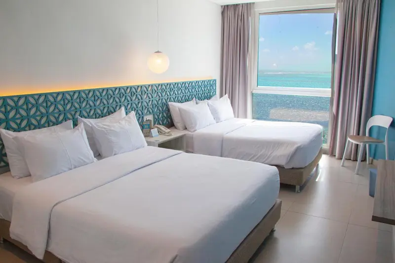 Chambre lumineuse avec deux lits simples et vue sur la mer.