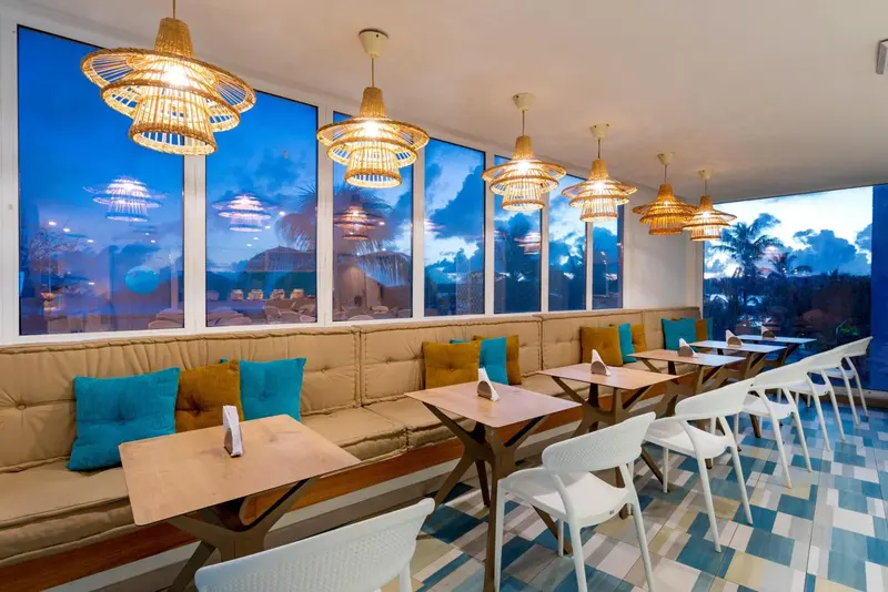 Une salle à manger lumineuse avec des tables et des banquettes confortables face à de grandes baies vitrées.