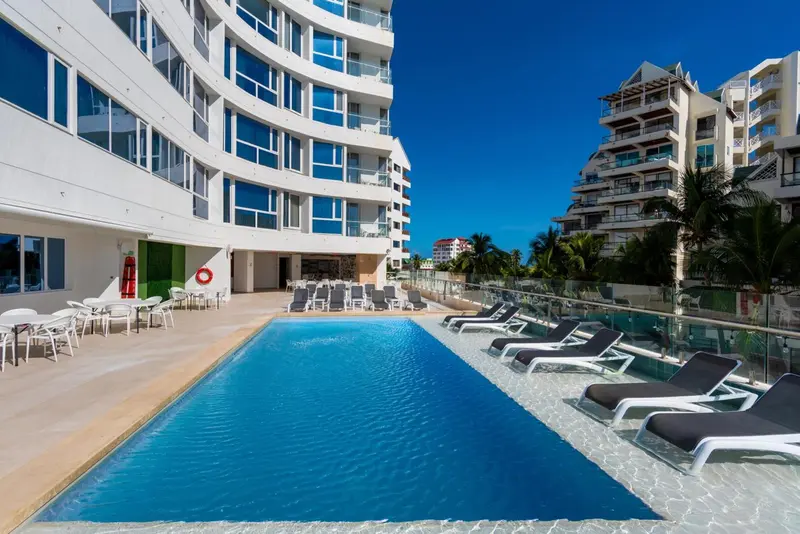 Une piscine rectangulaire bordée de transats devant un bâtiment blanc.