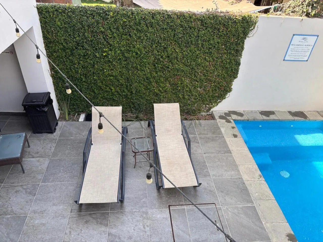 Deux transats gris sont placés au bord d'une piscine rectangulaire bleue.
