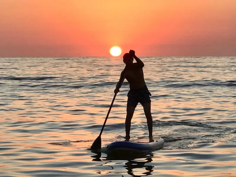 Silhouette d'une personne pratiquant le paddleboard au coucher du soleil sur une mer calme.