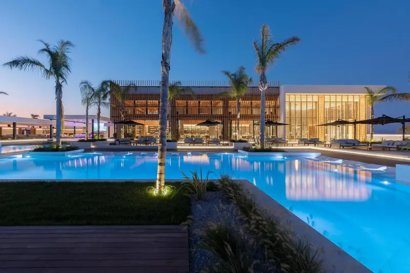 Vue d'une piscine illuminée devant un bâtiment moderne avec des palmiers.
