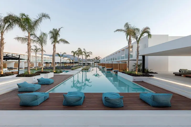 Une piscine rectangulaire bordée de transats et de palmiers.