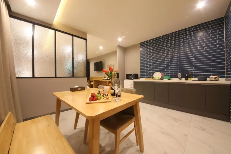 Une table en bois est dressée devant une cuisine équipée et un mur bleu.