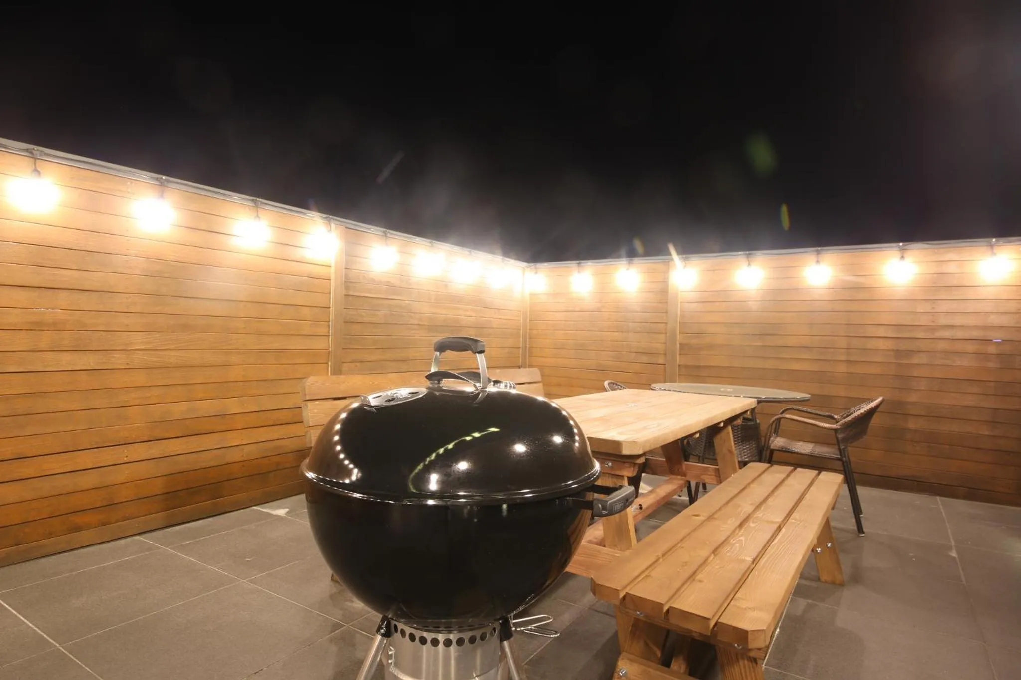Un barbecue et une table à manger sur une terrasse éclairée par des guirlandes lumineuses.