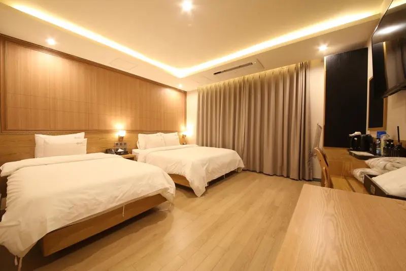 Chambre lumineuse avec deux lits simples et un coin bureau.