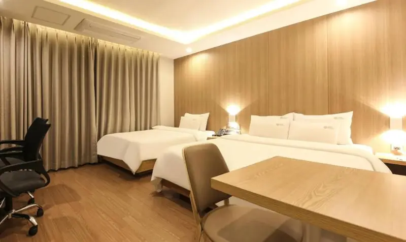 Une chambre d'hôtel lumineuse avec deux lits simples et un bureau.