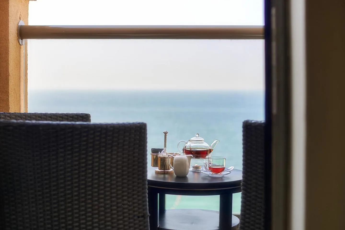 Une table avec une théière et des verres est placée sur un balcon avec vue sur la mer.