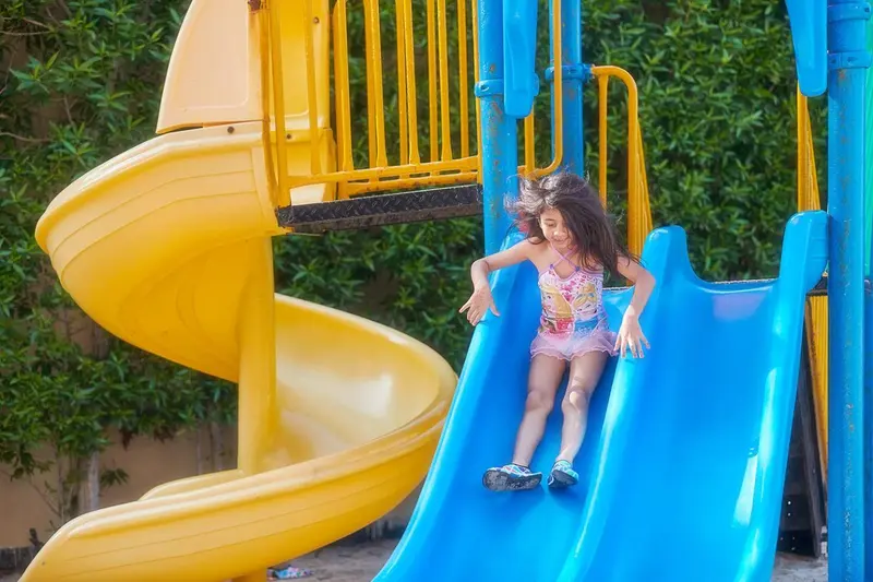 Une jeune fille descend un toboggan coloré sur une aire de jeux.