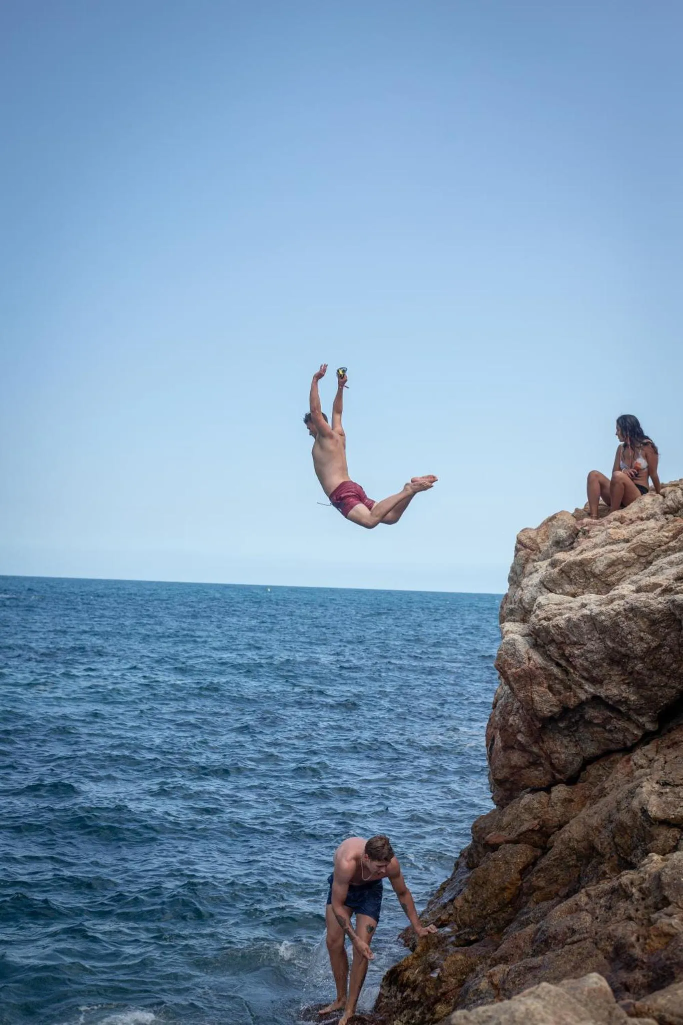 Une personne effectue une plongee spectaculaire depuis une falaise rocheuse en bord de mer.