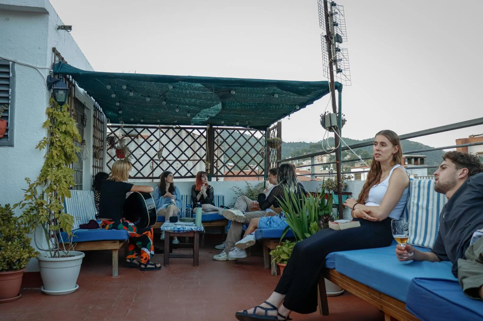 Un groupe de personnes discute sur une terrasse ombragée avec des canapés et des plantes.