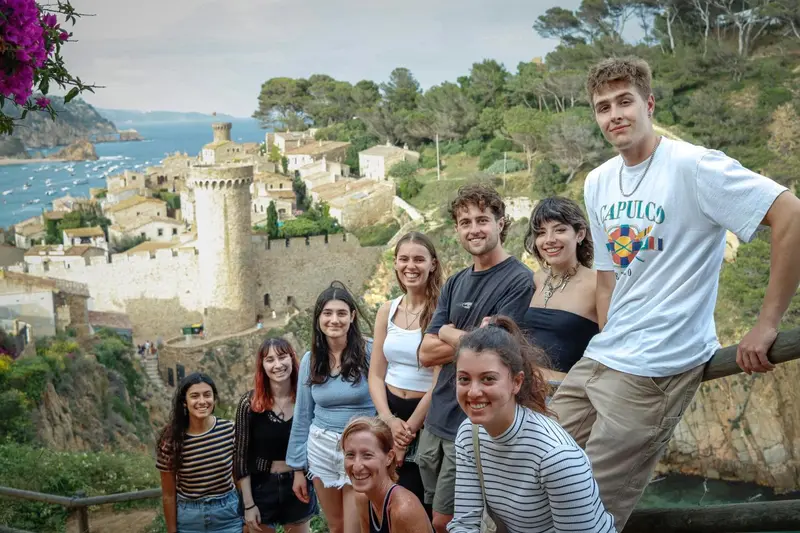 Groupe de jeunes adultes souriants posant sur une terrasse avec vue sur un village côtier.