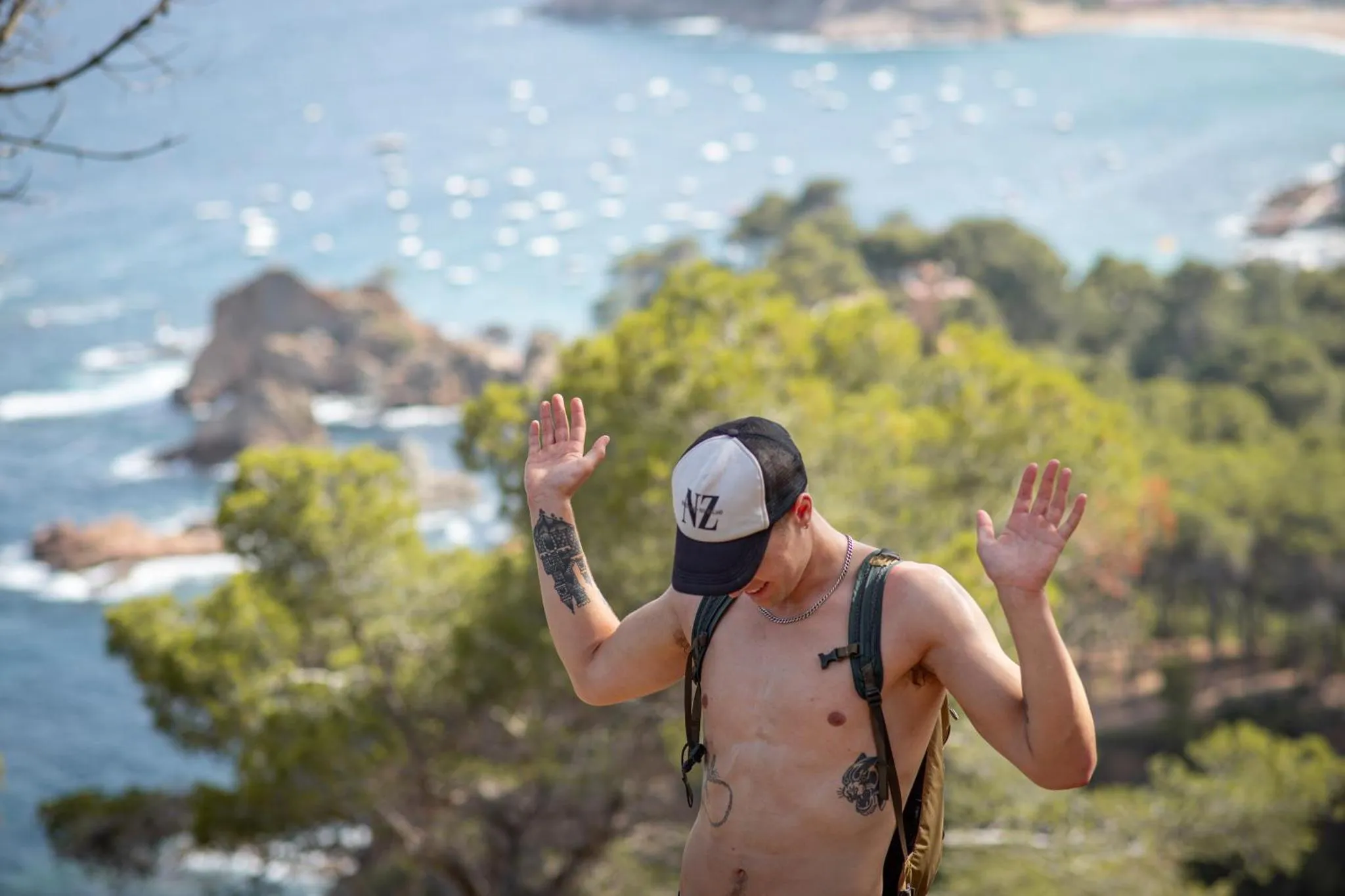 Un homme torse nu se tient face à la mer avec les bras levés.
