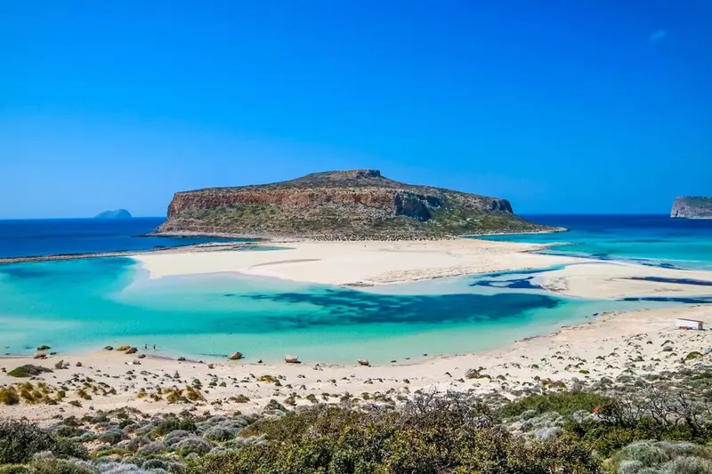 Vue aérienne d'une plage de sable blanc et d'eaux turquoise bordant une île rocheuse.