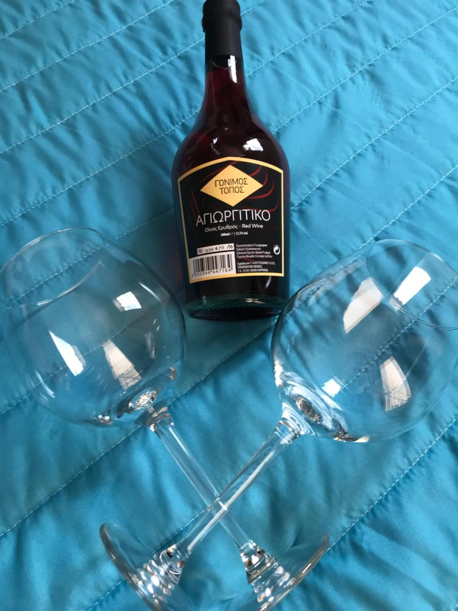Une bouteille de vin rouge et deux verres à vin reposent sur un tissu bleu.