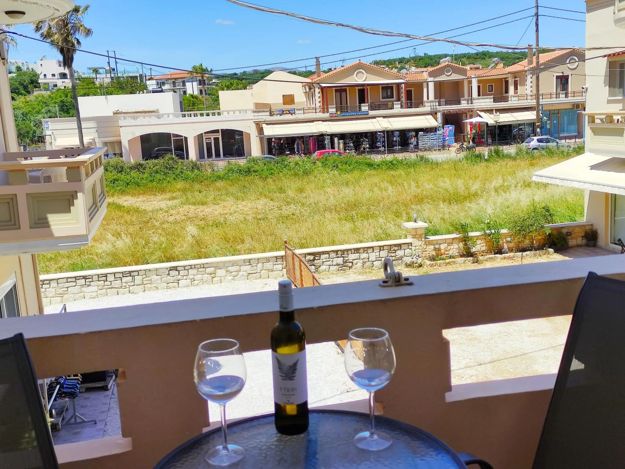Une table avec des verres et une bouteille de vin sur un balcon ensoleillé.