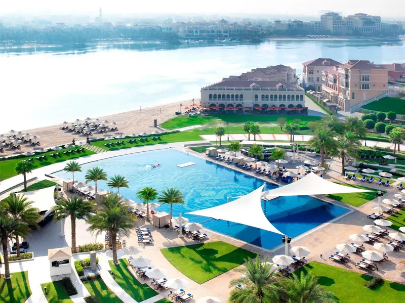Vue aérienne d'une grande piscine d'hôtel bordée de transats et de palmiers.