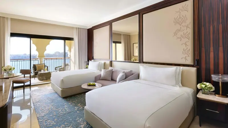 Chambre lumineuse avec deux lits et accès à une terrasse vue sur mer.