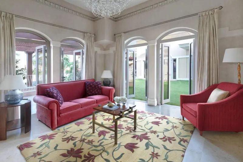 Un salon lumineux avec un canapé rouge et des fauteuils, ouvert sur une cour verdoyante.