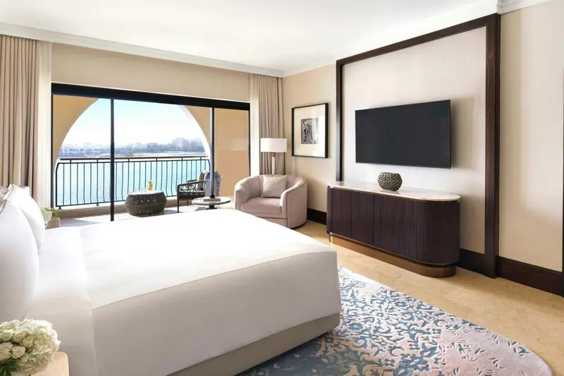 Une chambre lumineuse avec un grand lit et un accès à un balcon donnant sur la mer.