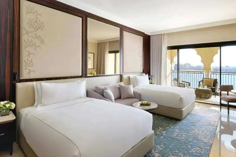 Chambre lumineuse avec deux lits et vue sur la mer par une baie vitrée.