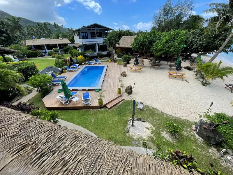Vue aérienne d'un complexe hôtelier avec piscine et transats sur une plage de sable blanc.