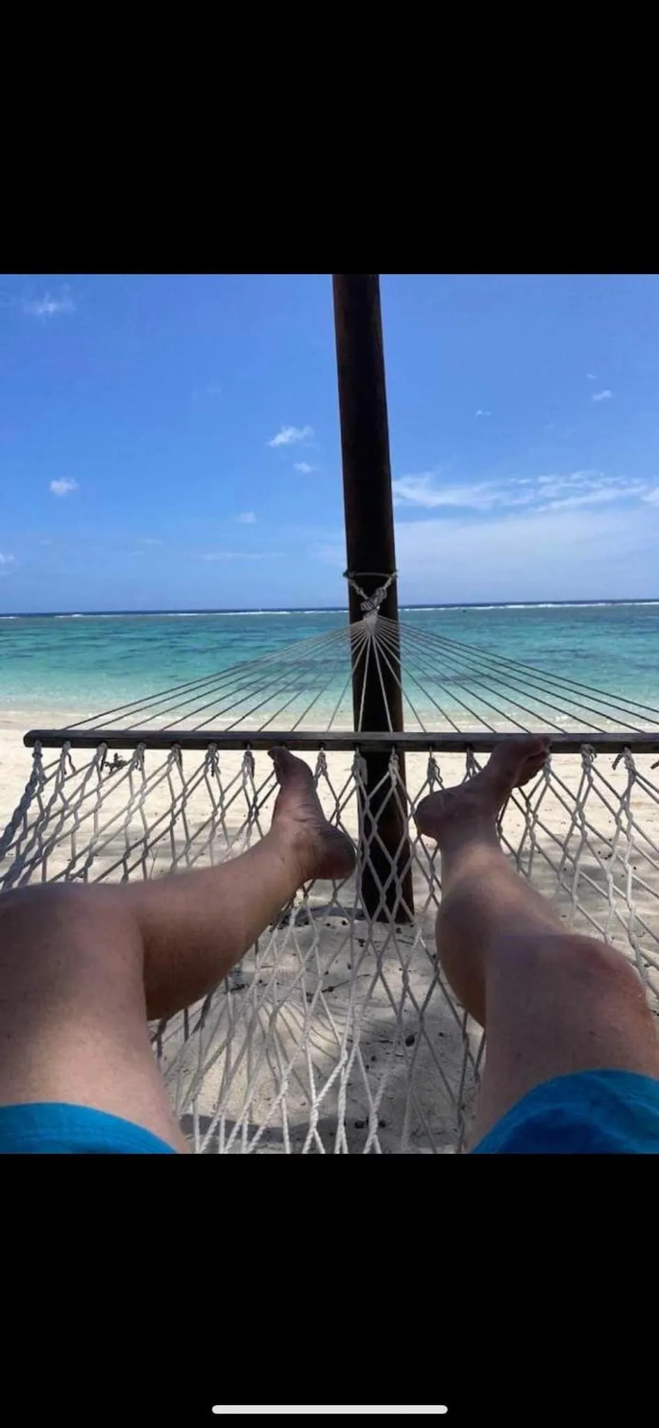 Pieds reposant dans un hamac sur une plage de sable blanc face à la mer.