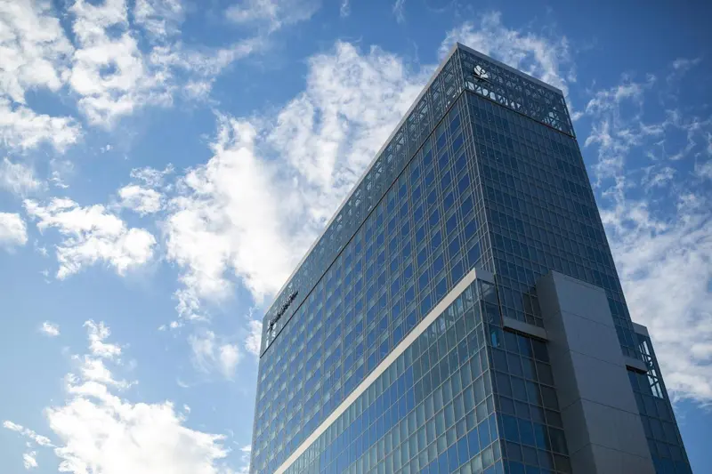 Imposant bâtiment moderne aux nombreuses fenêtres reflétant le ciel bleu.