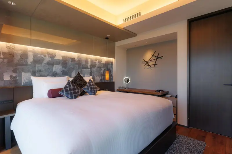 Une chambre lumineuse avec un grand lit recouvert d'une courtepointe blanche et de coussins décoratifs.