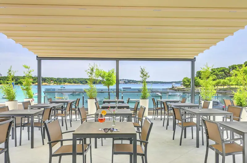 Terrasse ombragée avec tables et chaises donnant sur une vue maritime.