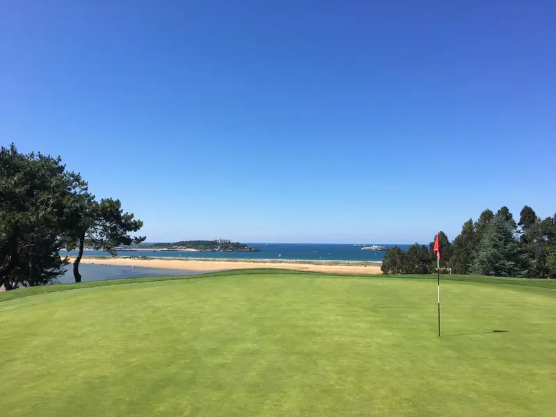 Un terrain de golf vert s'étend vers une plage de sable fin et une mer bleue.