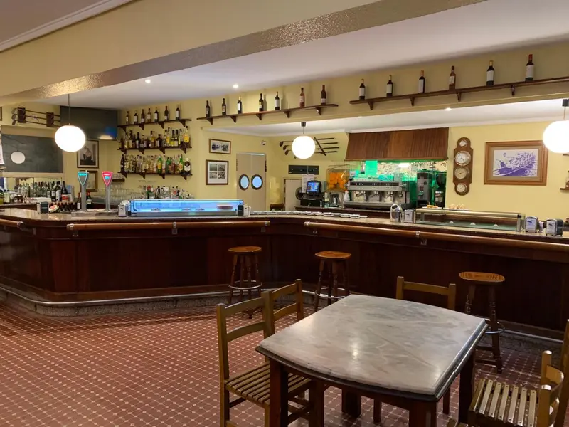 Un comptoir de bar en bois avec des bouteilles et des tabourets, dans une salle décorée.