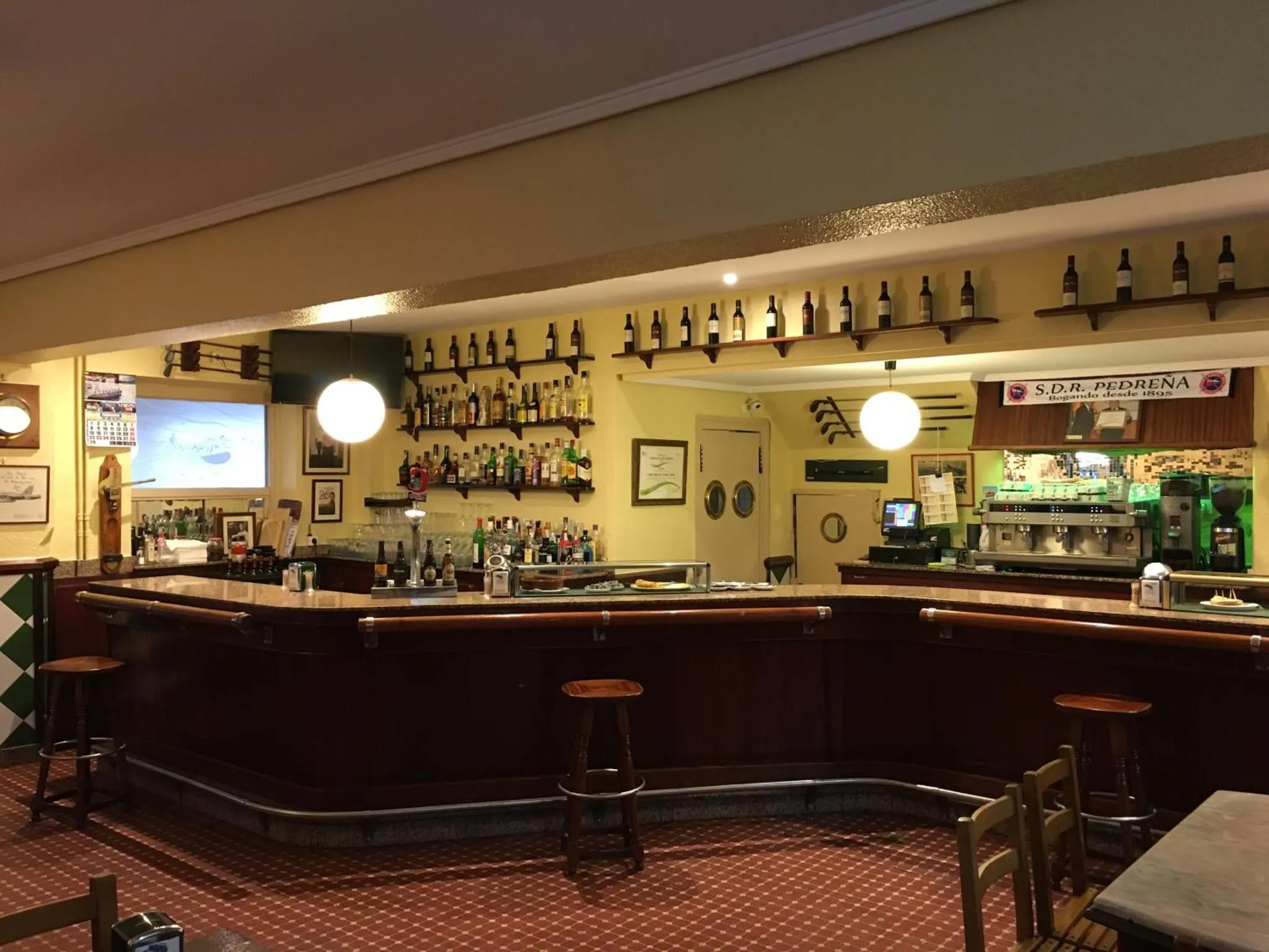 Un comptoir de bar en bois sombre avec des tabourets, des bouteilles exposées et un fond décoré.