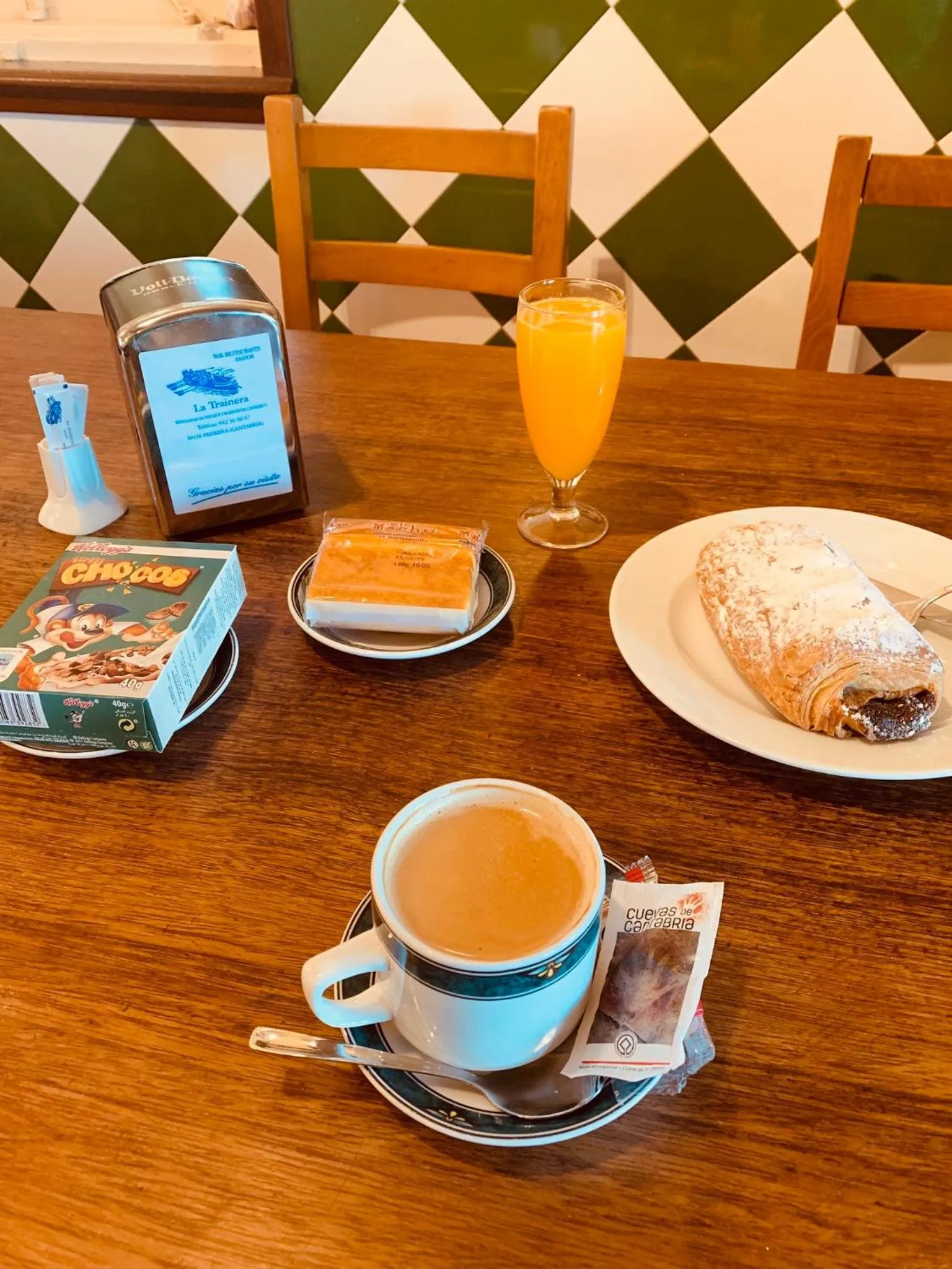 Une table en bois présente un petit-déjeuner avec une boisson orange, un café et des pâtisseries.