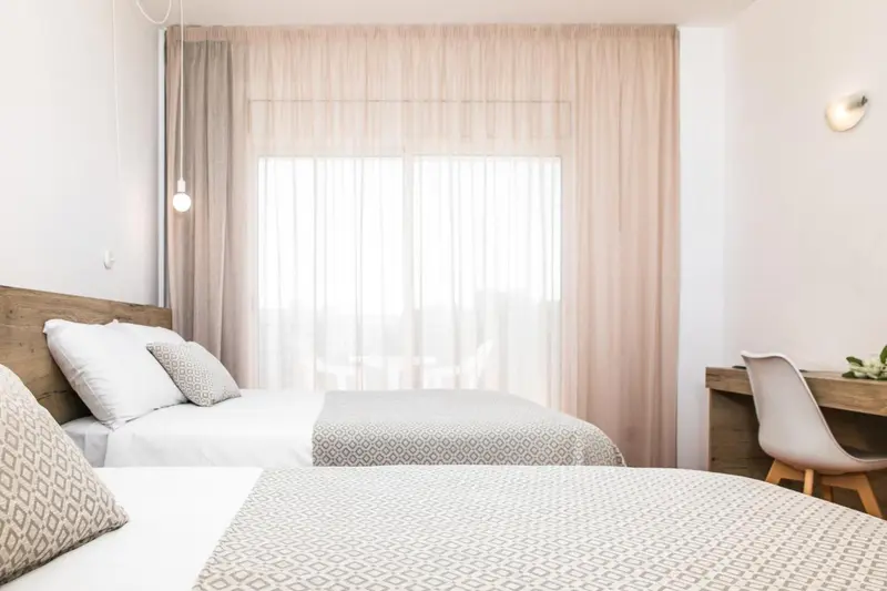 Une chambre lumineuse avec deux lits simples et un bureau.