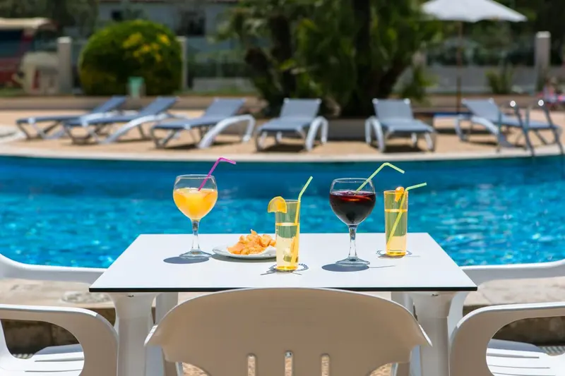 Des cocktails colorés et des amuse-gueules sont servis sur une table près d'une piscine ensoleillée.