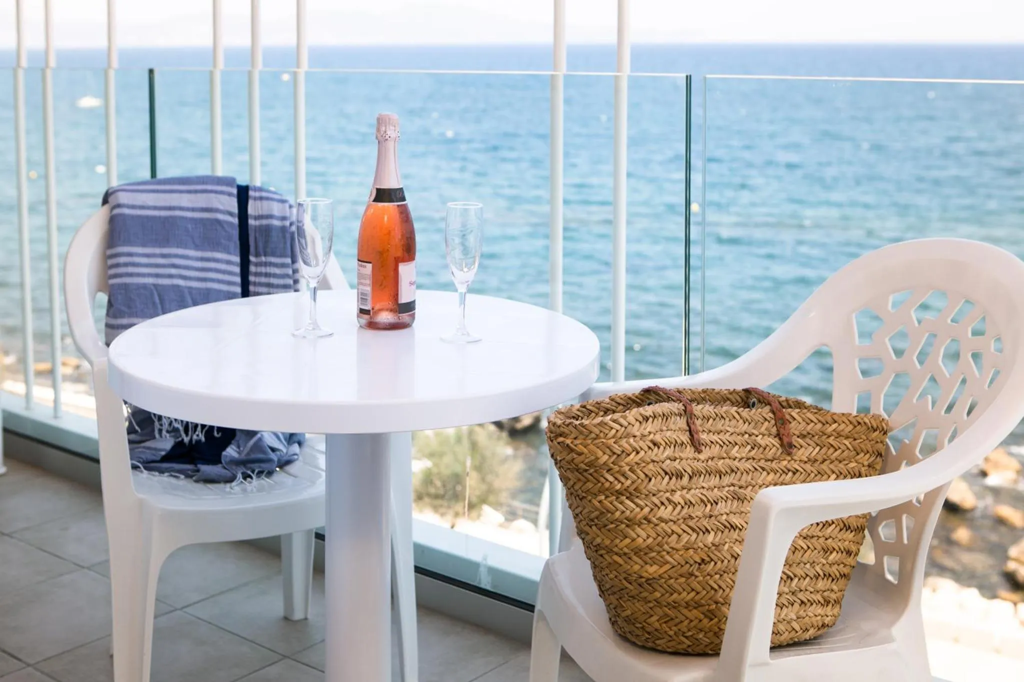 Une table ronde avec des boissons et des verres sur une terrasse ensoleillée avec vue sur la mer.