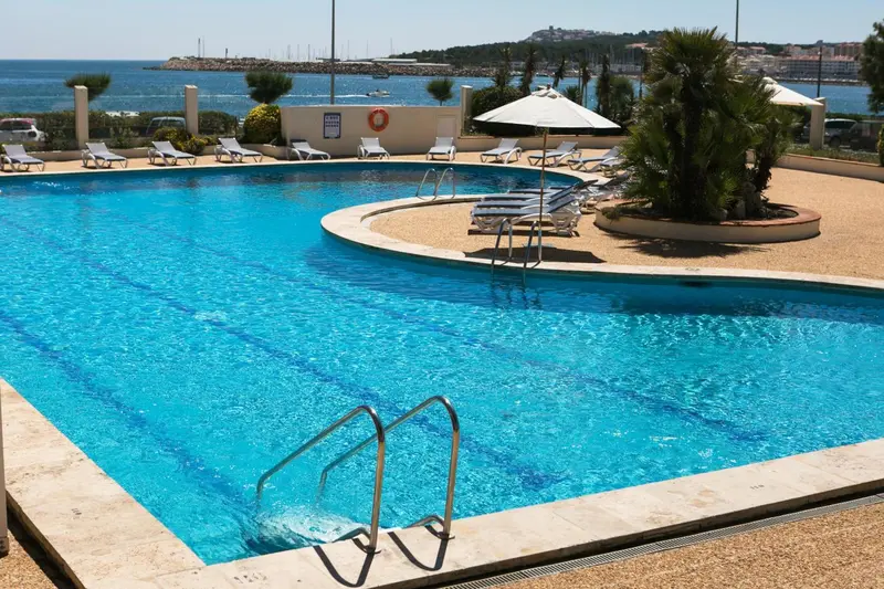 Une piscine bleue bordée de transats sous le soleil.