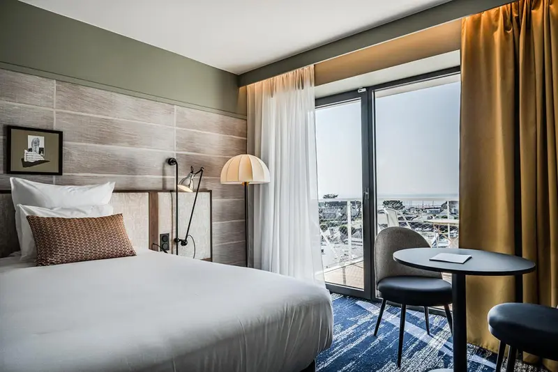 Une chambre lumineuse avec un lit et un coin salon donnant sur une vue urbaine.