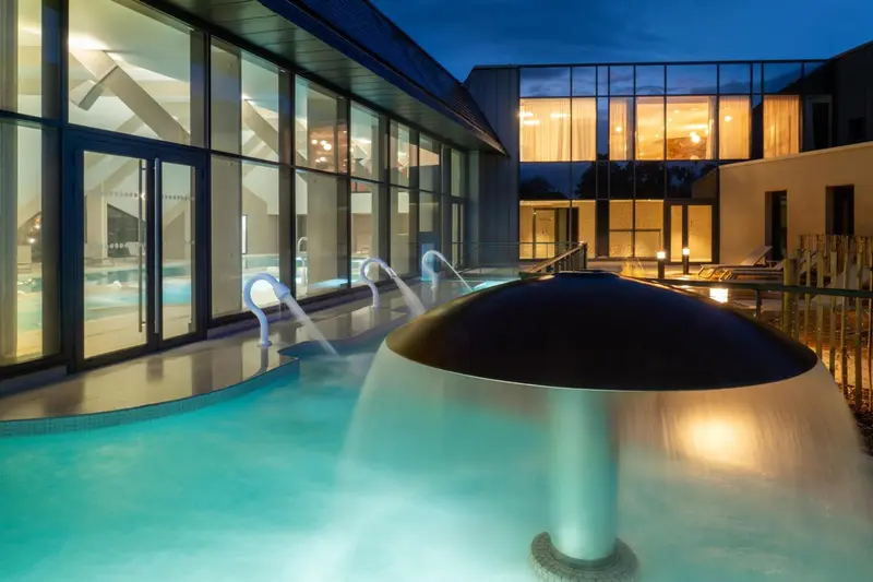 Bassin extérieur illuminé avec jets d'eau et structure moderne.