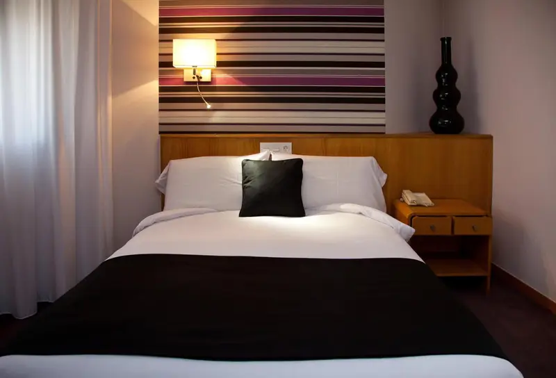 Une chambre lumineuse avec un lit recouvert d'une couverture noire et de coussins.